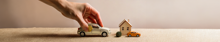 Hand grabbing a mini car with a mini house nearby